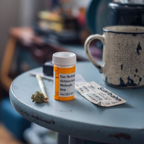 Tisch mit halb leerer Medikamentenflasche, Cannabisjoint und abgenutztem Saarbahn-Ticket.