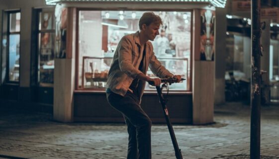 Student fährt unsicher auf E-Scooter vor beleuchtetem Dönerimbiss