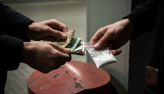 Nahaufnahme des schnellen Austauschs von zerknüllten Geldscheinen gegen einen winzigen, durchscheinenden Plastikbeutel mit weißem Pulver.