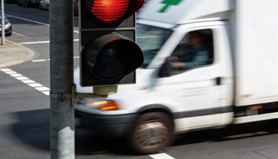Ein weißes Apotheken-Lieferfahrzeug fährt eilig bei rot leuchtender Ampel über die Haltelinie einer Kreuzung.
