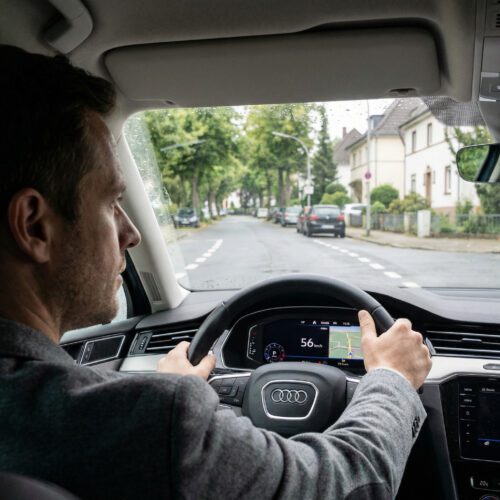 Die Hände eines fokussierten Fahrers umgreifen fest das Lenkrad eines fahrenden Autos auf einer markierten Straße.
