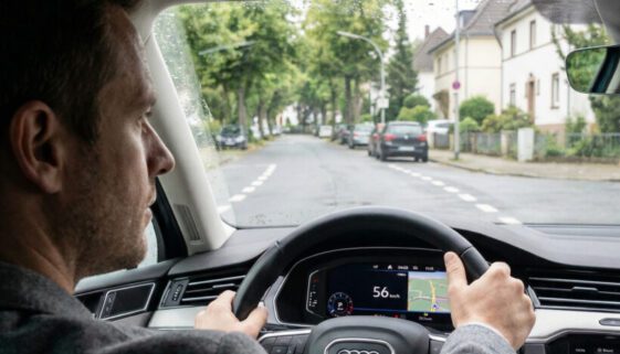 Die Hände eines fokussierten Fahrers umgreifen fest das Lenkrad eines fahrenden Autos auf einer markierten Straße.