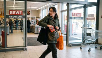 Frau am Supermarktausgang schiebt hastig unbezahlte Ware in ihre Tasche und blickt sich nervös um.